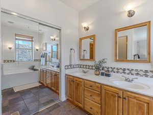 Full bathroom with double vanity, stone tile flooring, a bathtub, and tasteful backsplash