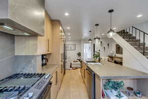 Kitchen with light wood finish cabinets, stainless steel appliances, a spacious island, light countertops, and light wood-style flooring