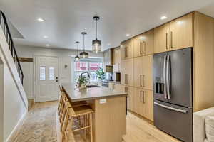 Kitchen with light wood finish cabinets, stainless steel appliances, a kitchen island with sink, and light wood-style floors