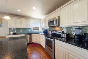 Kitchen featuring stainless steel appliances, dark stone counters, dark wood-type flooring, a textured ceiling, and backsplash