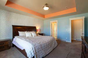 Bedroom with a tray ceiling, dark carpet, and wallpapered walls