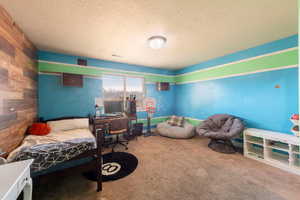 Carpeted bedroom with a textured ceiling, wood walls, and an office area