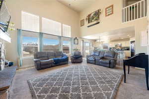 Living area with a stone fireplace, light carpet, a chandelier, and a high ceiling