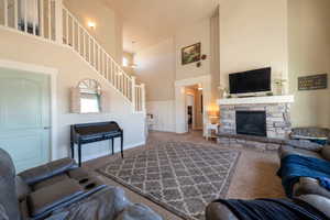 Living room featuring a high ceiling, carpet floors, a stone fireplace, and wainscoting