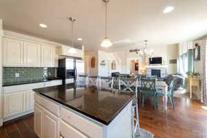 Kitchen with open floor plan, a breakfast bar area, dark wood-style floors, stainless steel refrigerator with ice dispenser, and dark stone countertops