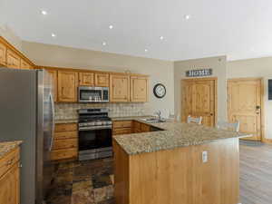 Kitchen with a peninsula, stainless steel appliances, light stone counters, decorative backsplash, and recessed lighting