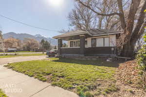 View of front facade with a mountain view, a porch, dirt driveway, and a shingled roof