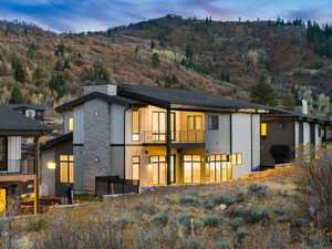 Back of house with stone siding, a balcony, a mountain view, and a chimney
