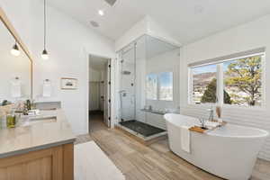 Full bath featuring a freestanding tub, a shower stall, double vanity, vaulted ceiling, and wood finish floors