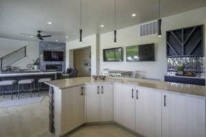 Kitchen with open floor plan, light stone countertops, ceiling fan, a fireplace, and hanging light fixtures