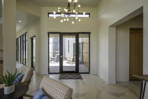 Foyer entrance featuring hanging lights, light marble finish floors, and a high ceiling