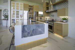 Kitchen with light marble finish flooring, light wood finish cabinets, light stone countertops, and high end appliances