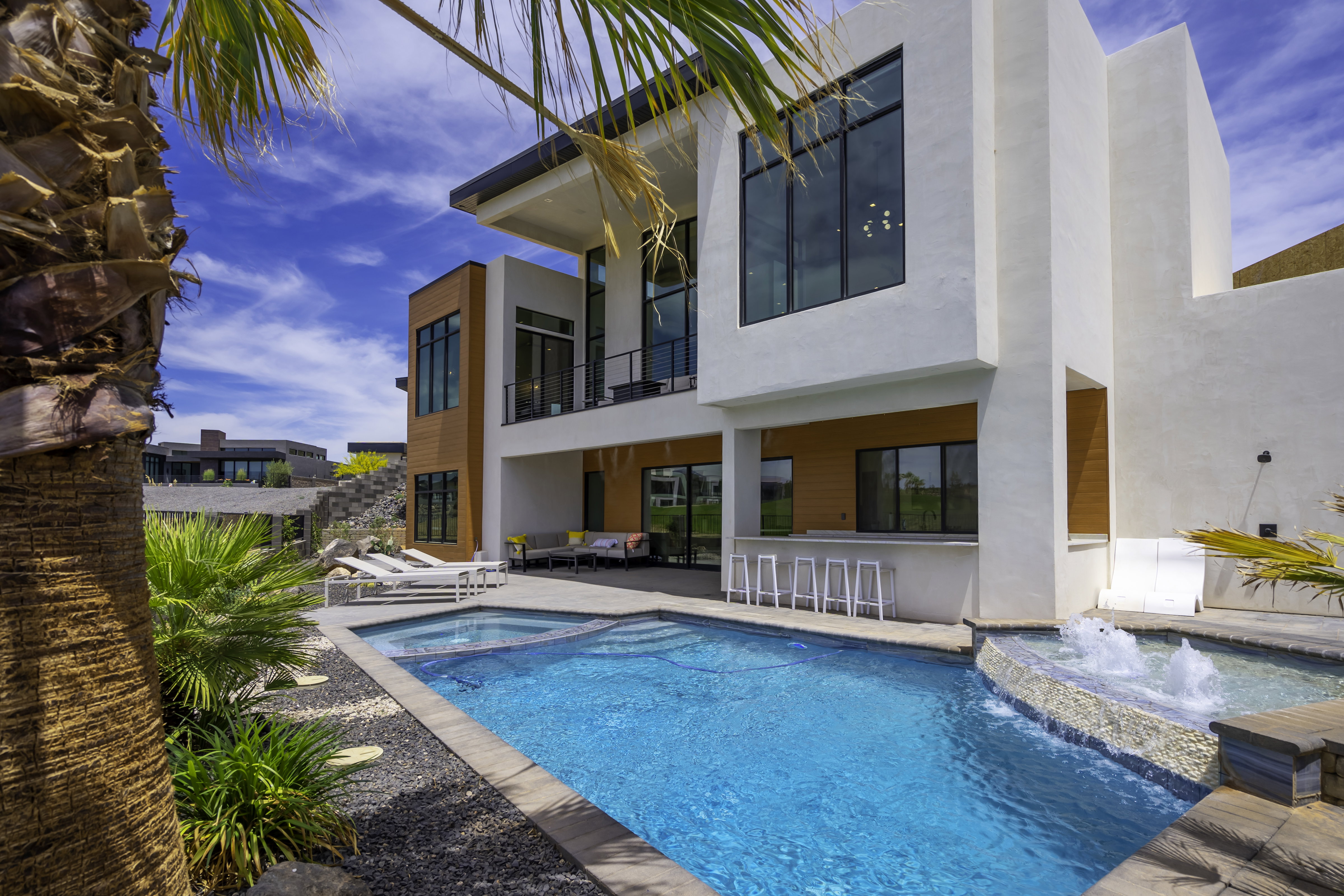 Rear view of house featuring a balcony, stucco siding, a patio area, a pool with connected hot tub, and an outdoor lounge area with bar