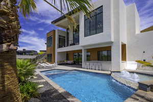 Rear view of house featuring a balcony, stucco siding, a patio area, a pool with connected hot tub, and an outdoor lounge area with bar