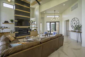Living room with a fireplace, light marble finish floors, a high ceiling, and a chandelier