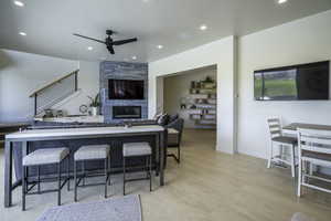 Kitchen featuring a tile fireplace, a ceiling fan, open floor plan, recessed lighting, and a breakfast bar