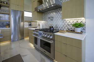Kitchen featuring extractor fan, light wood finish cabinetry, high end appliances, modern cabinets, and light stone countertops