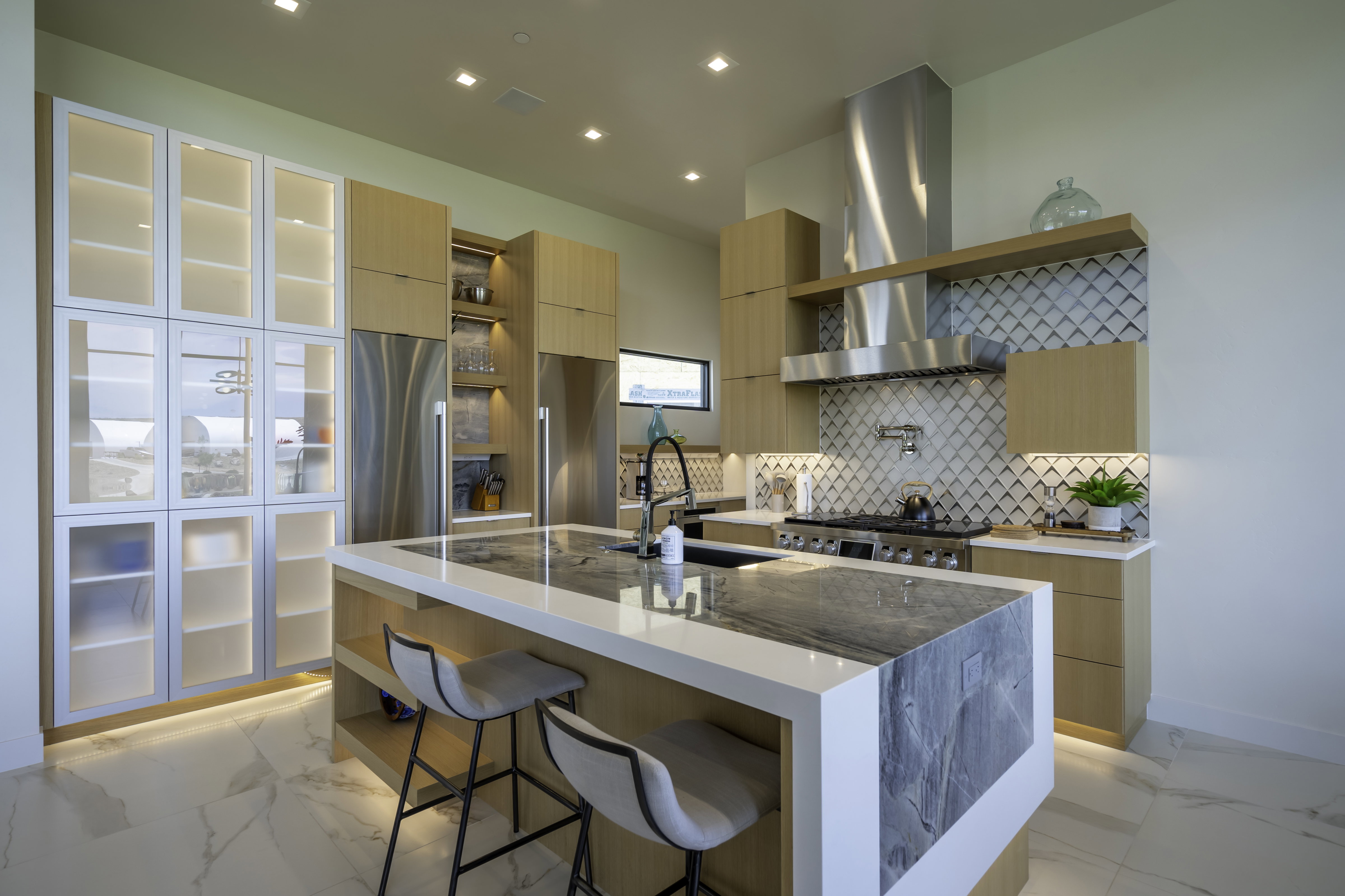 Kitchen with light wood finish cabinets, light stone counters, stainless steel appliances, a kitchen island with sink, and recessed lighting