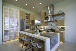 Kitchen with light wood finish cabinets, light stone counters, stainless steel appliances, a kitchen island with sink, and recessed lighting