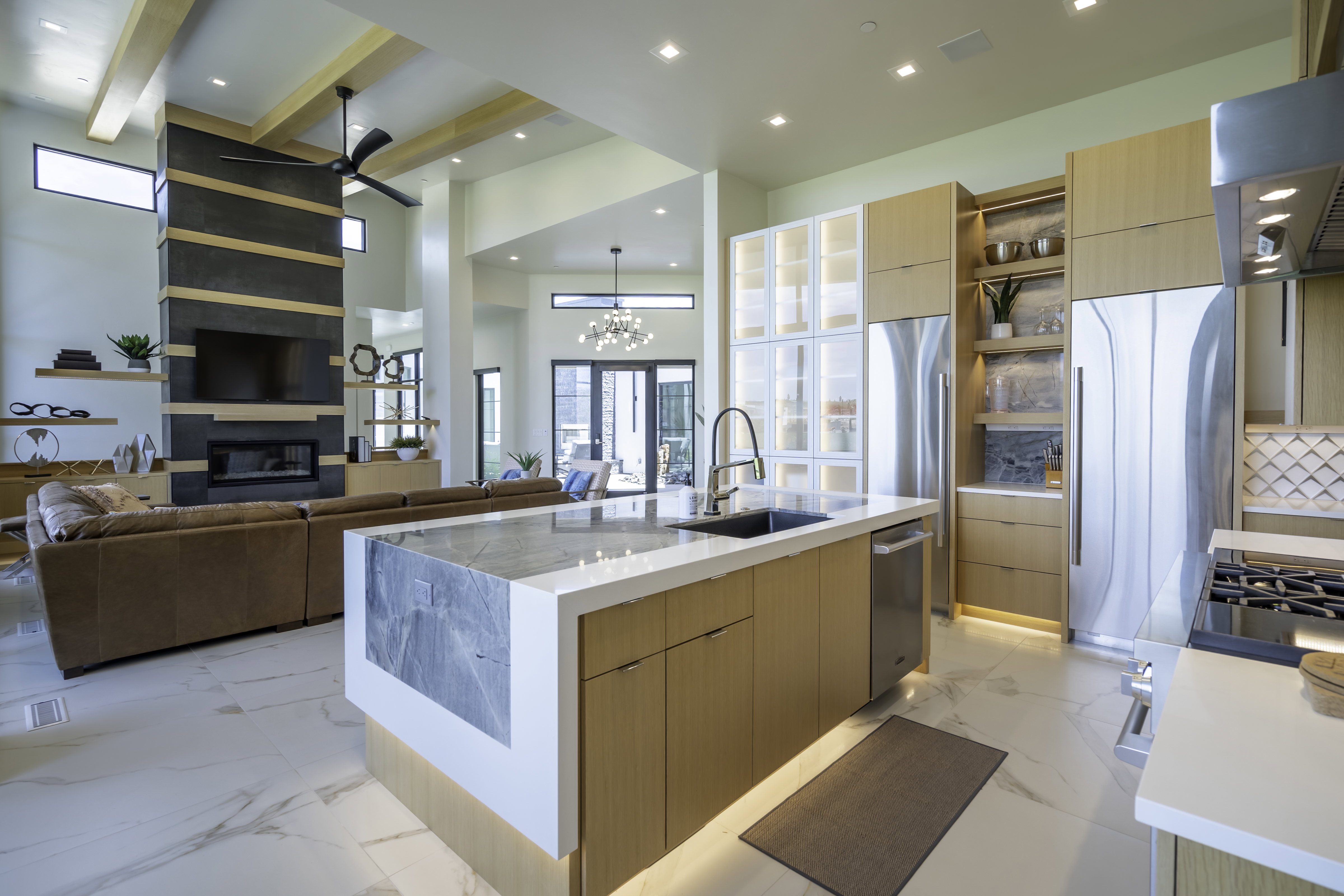 Kitchen featuring modern cabinets, light wood finish cabinetry, a center island with sink, extractor fan, and light stone counters