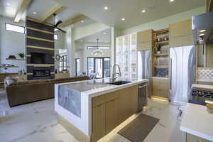 Kitchen featuring modern cabinets, light wood finish cabinetry, a center island with sink, extractor fan, and light stone counters
