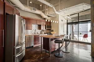 Kitchen with stainless steel appliances, finished concrete floors, a center island, light stone countertops, and backsplash