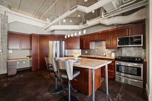 Kitchen featuring stainless steel appliances, a breakfast bar, a center island, a high ceiling, and concrete floors