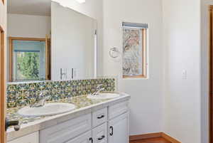 Full bathroom with double vanity, tasteful backsplash, and light wood finished floors
