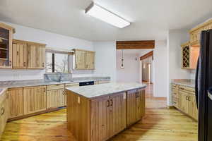 Kitchen with a kitchen island, light wood finished floors, black appliances, and light wood finish cabinetry