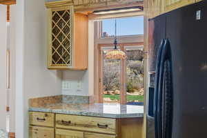 Kitchen with black fridge, light wood finish cabinetry, and light stone counters