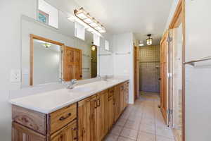 Full bath featuring double vanity, light tile patterned floors, and a shower stall