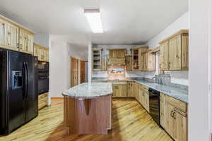 Kitchen with black appliances, light wood finished floors, light stone counters, light wood finish cabinets, and a textured ceiling