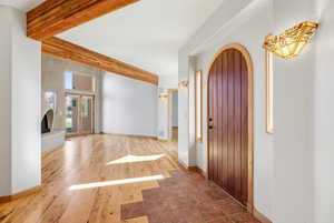 Foyer with beam ceiling, arched walkways, light wood-style floors, and a fireplace