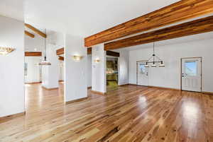 Unfurnished living room with light wood-type flooring, beam ceiling, and suspended lighting