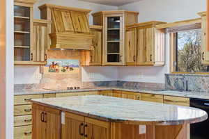 Kitchen with black appliances, glass fronted cabinets, light stone countertops, a kitchen island, and open shelves