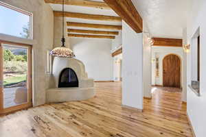 Unfurnished living room with a glass covered fireplace, beamed ceiling, light wood-style flooring, and arched walkways