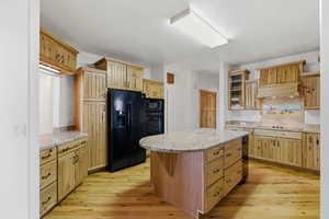 Kitchen with black appliances, light stone counters, glass insert cabinets, and light wood-style flooring