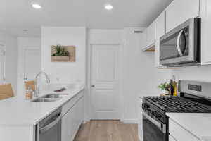 Kitchen featuring stainless steel appliances, a peninsula, white cabinets, light stone countertops, and light wood finished floors
