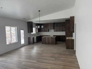 Kitchen with dark wood finish cabinets, vaulted ceiling, dark wood finished floors, decorative light fixtures, and a center island