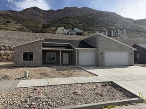View of front facade with concrete driveway, stone siding, an attached garage, a mountain view, and covered porch