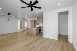 Kitchen with open floor plan, gas stove, a kitchen island with sink, ceiling fan, and light wood-type flooring