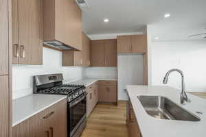 Kitchen with stainless steel gas stove, light wood-style floors, modern cabinets, light stone counters, and recessed lighting