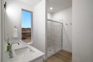 Full bath with double vanity, light wood-type flooring, and a stall shower