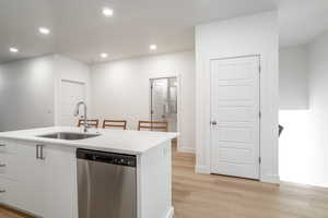 Kitchen featuring stainless steel dishwasher, a kitchen island with sink, recessed lighting, light wood-style floors, and white cabinetry