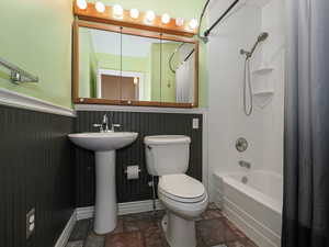 Bathroom with shower / tub combo with curtain, stone tile floors, and wainscoting