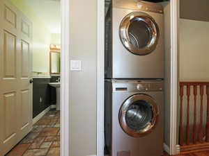 Laundry area with stacked washer / drying machine and dark stone finish floors