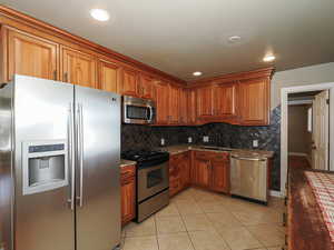 Kitchen with stainless steel appliances, light stone countertops, wood finish cabinets, light tile patterned flooring, and recessed lighting