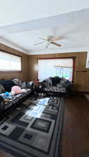 Living room with wooden walls, dark wood-type flooring, healthy amount of natural light, and a ceiling fan