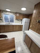 Kitchen featuring wood finish cabinetry, light flooring, light countertops, freestanding refrigerator, and wallpapered walls