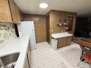Kitchen with light floors, light countertops, wood finish cabinetry, freestanding refrigerator, and wooden walls